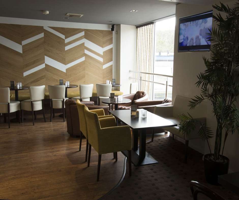 Interior of Oblo Bar and Bistro featuring wood floors, white walls, brown furniture, a wall-mounted TV, and a potted plant in the corner.