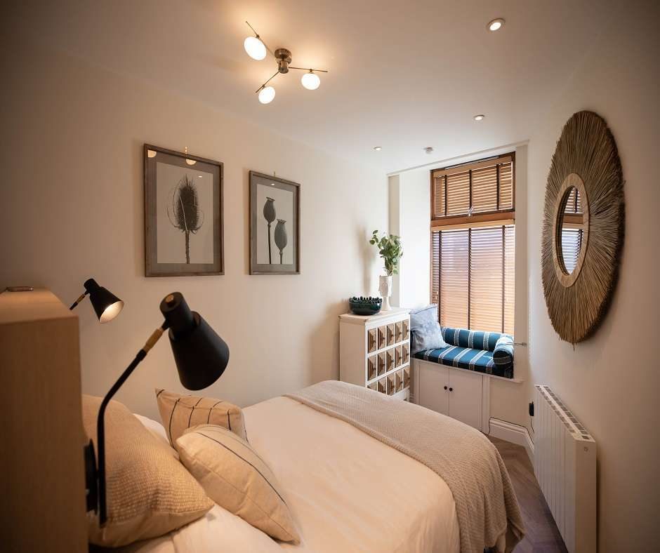 A holiday let room design with bed, two bedlights two picture frames and a wall mirror