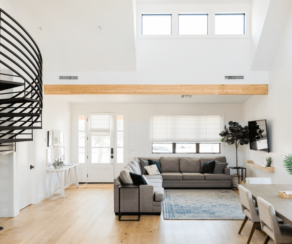 There is a photo of a living room with a couch, coffee table, rug, and plants. There is also a spiral staircase leading to a second floor.