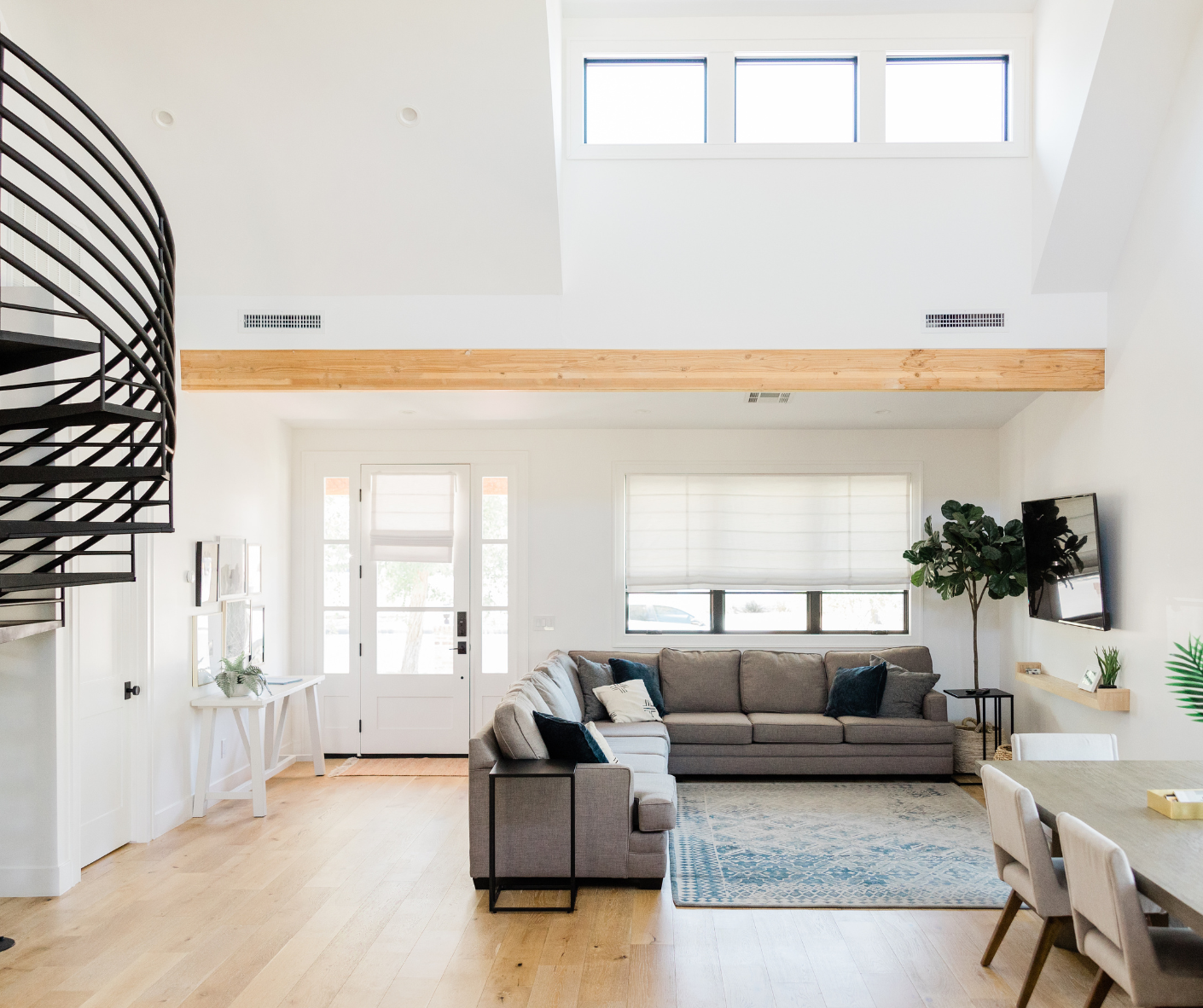 There is a photo of a living room with a couch, coffee table, rug, and plants. There is also a spiral staircase leading to a second floor.