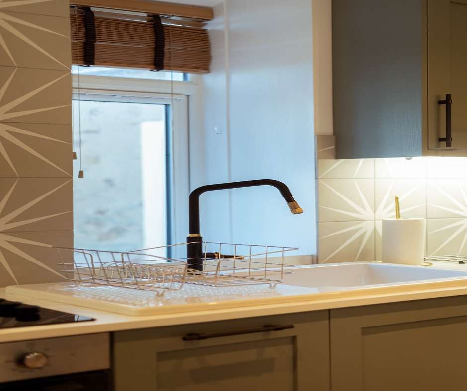 Close-up of a kitchen sink with a black faucet, neutral-toned backsplash tiles, and modern cabinetry.