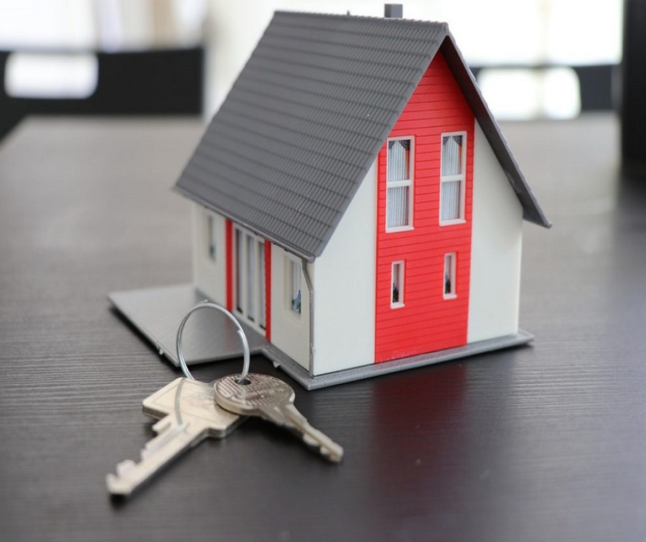 The image is of a small house with a red roof and white walls sitting on a table next to some keys. The house has a sign that says "Small Property Owners Looking to Increase Their ROI".